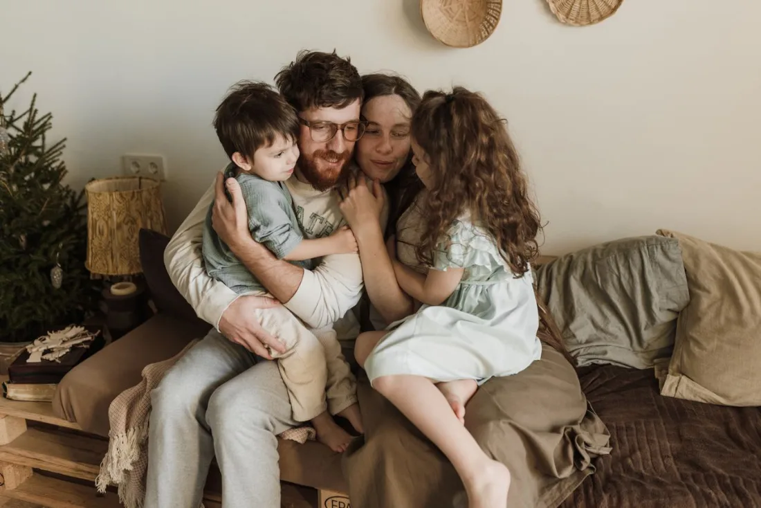 Un padre y una madre abrazan a sus dos hijos pequeños en el sofá de su casa